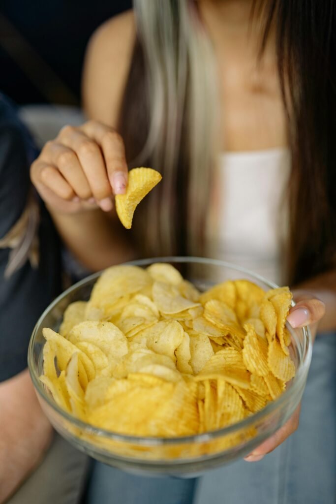Foods That Are Toxic To DOGS! - BE INFORMED 28 Young woman enjoying a bowl of crispy potato chips, highlighting snack time delight.